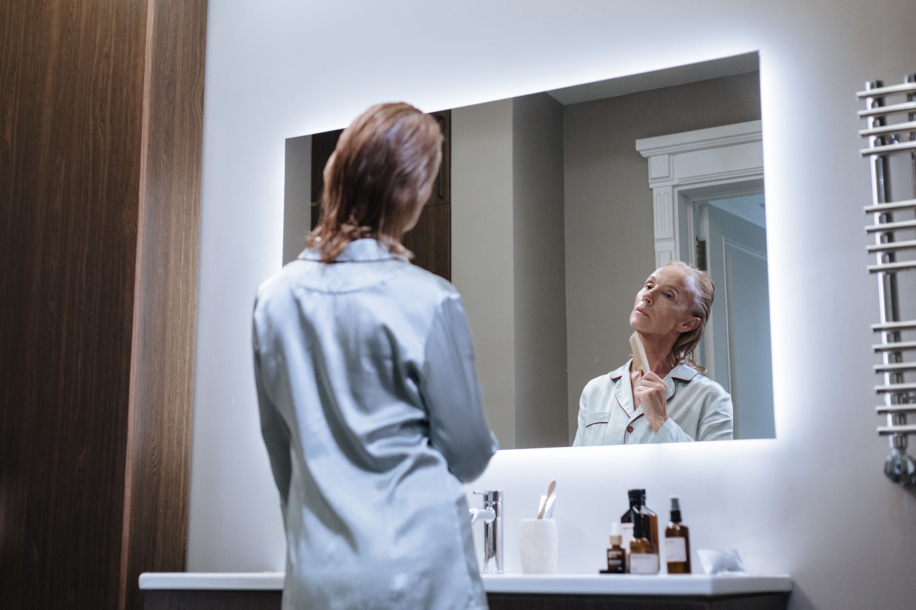 a low angle view of a senior adult looking at mirror during self care in bathroom