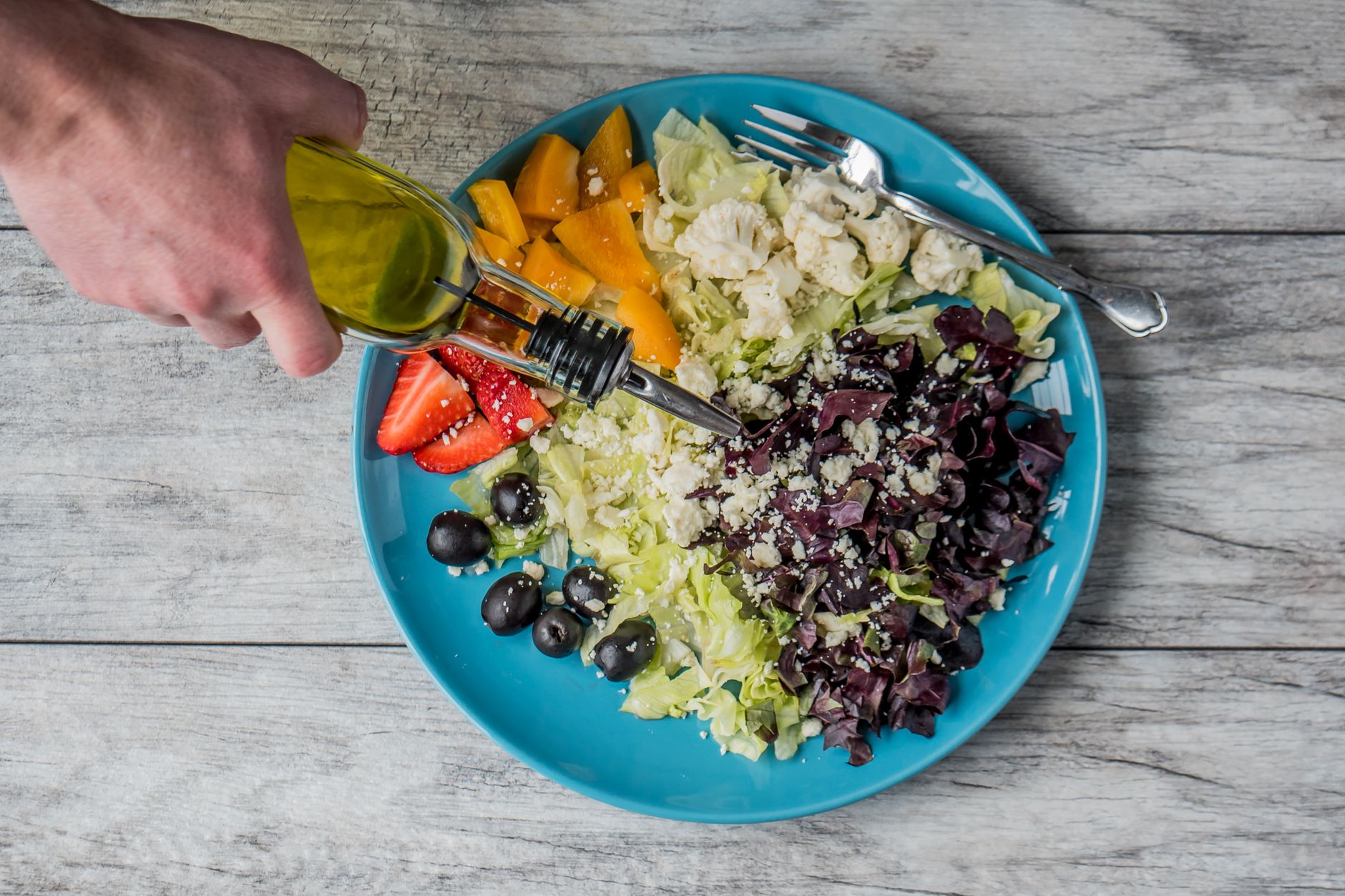 person pouring vegetable oil on vegetable salad